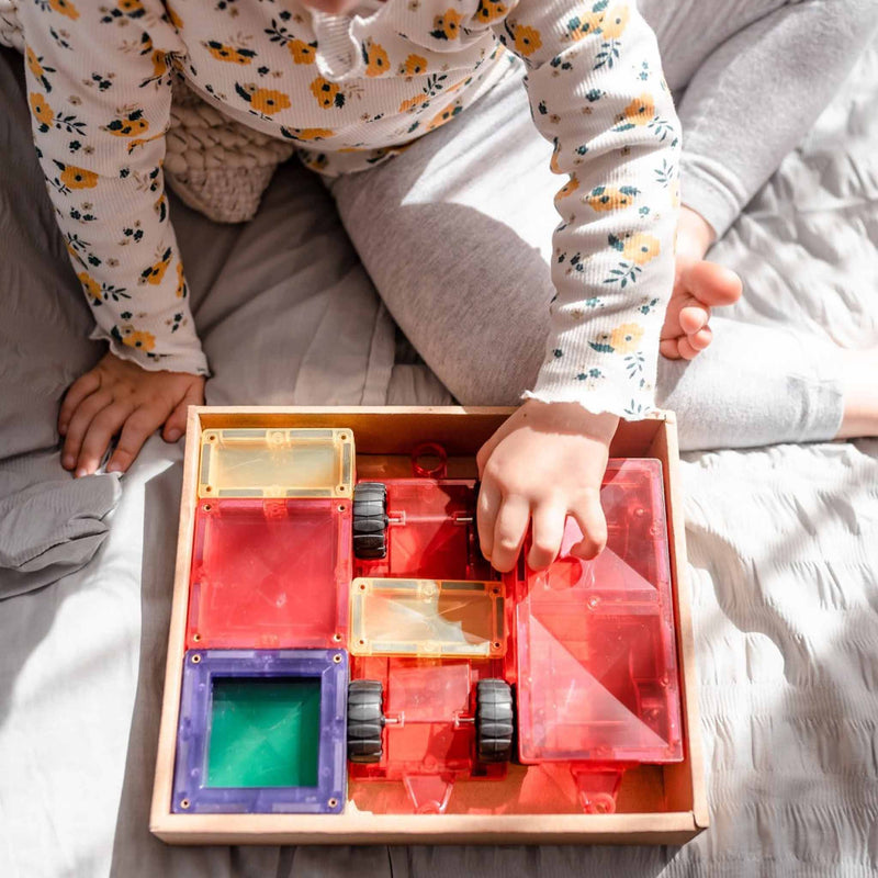Child playing with a transparent connetix game geometric shapes set on Connetix magnetic tiles on  a bed