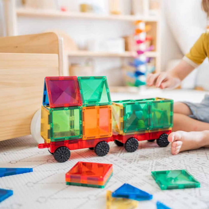 Colorful transparent magnetic building blocks on a child's lap with a blurred background of toys and a child playing connetix board Connetix magnetic tiles