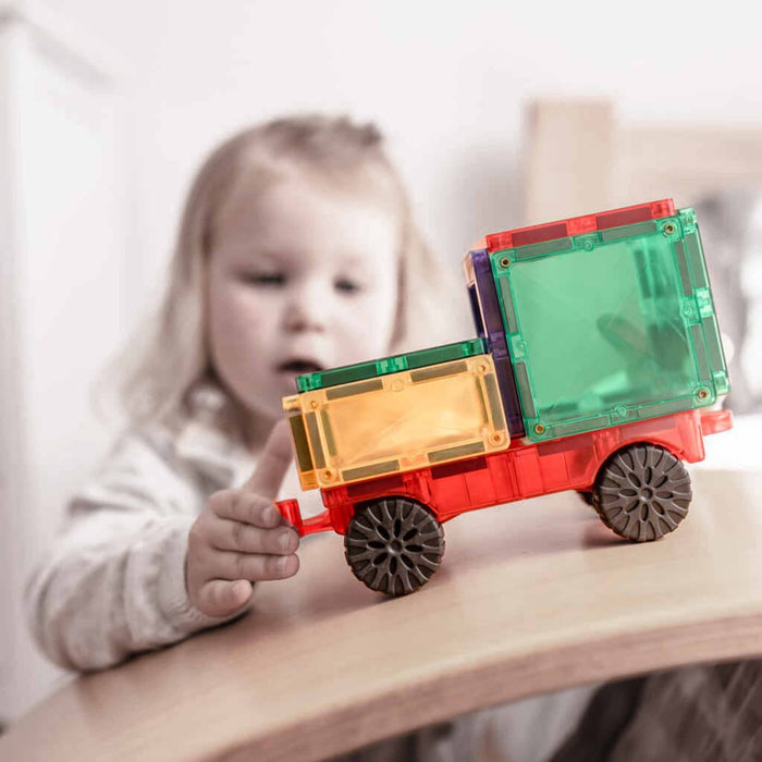 Child playing with a colorful toy truck on a wooden surface Connetix magnetic tiles