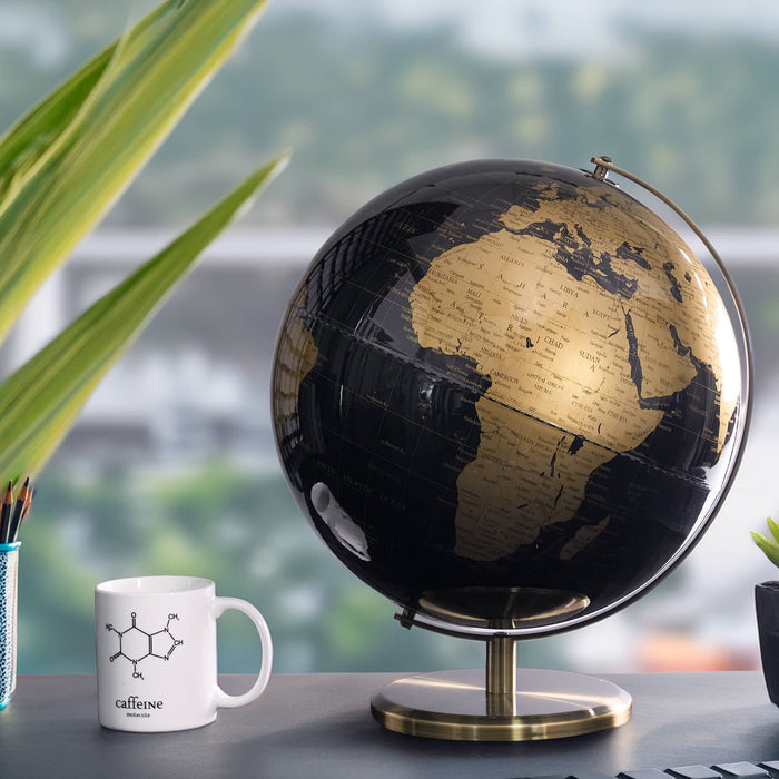 Black and gold globe on a desk with a white mug featuring chemical structure diagram.