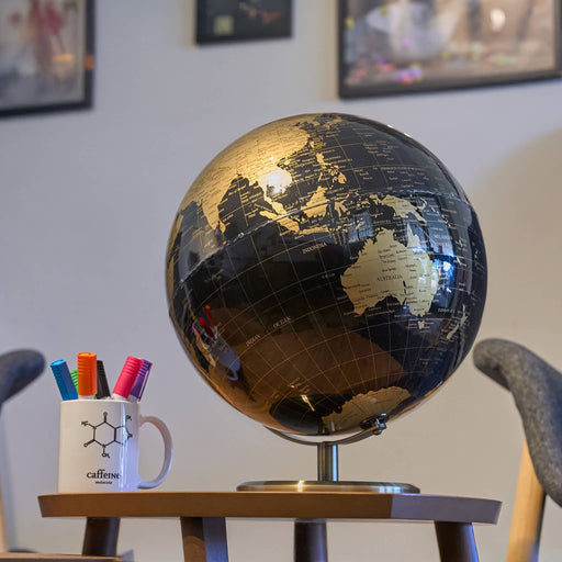 Globe on a stand with a mug containing pens and markers in a room setting.