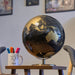 Globe on a stand with a mug containing pens and markers in a room setting.