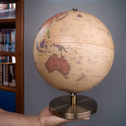 Hand holding a vintage-style globe with a bookshelf in the background