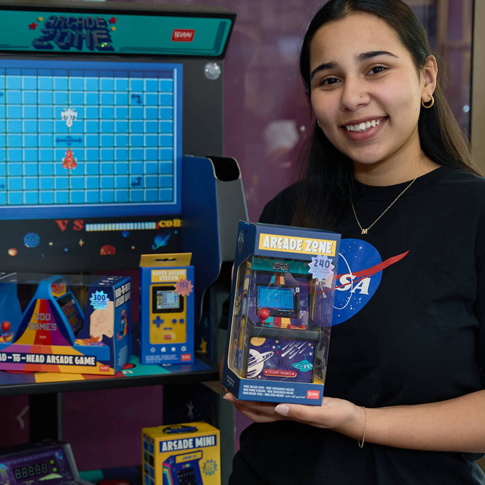 Woman holding a packaged arcade game in front of an arcade machine