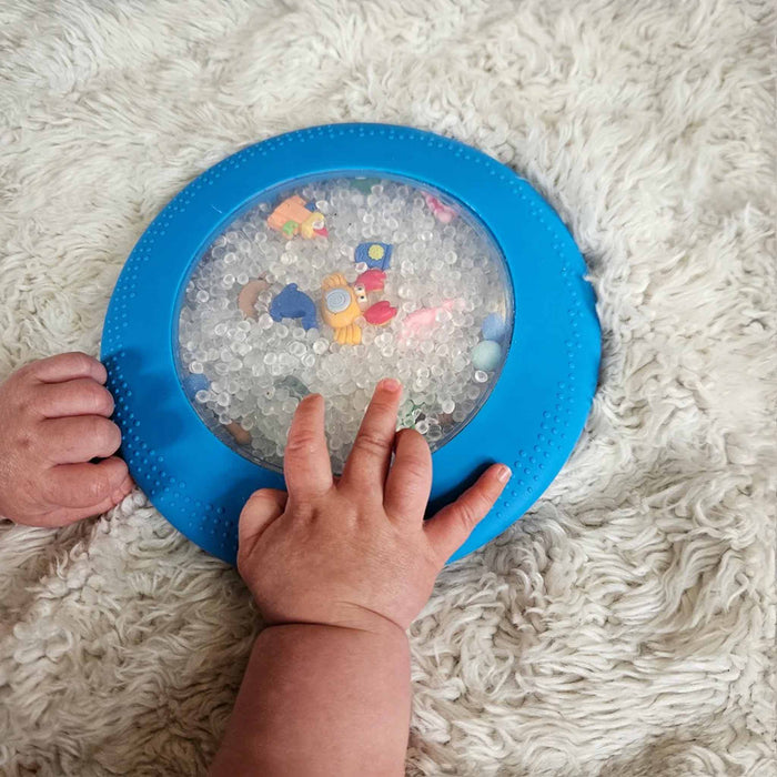 Child's hands holding a blue frisbee with a transparent center featuring colorful animal shapes on a white fluffy surface.