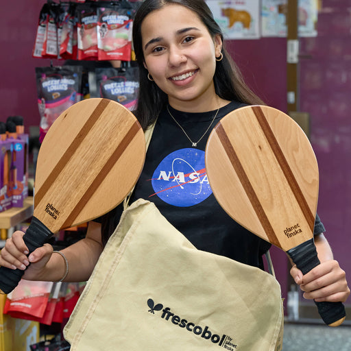 Person holding two wooden paddle sports products with a NASA shirt in a store setting