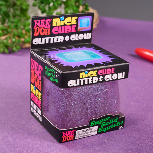 Box of Nee Doh Nice Cube Clitter & Glow on a purple surface with greenery in the background