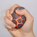 Hand squeezing a stress ball with lava design on a plain background