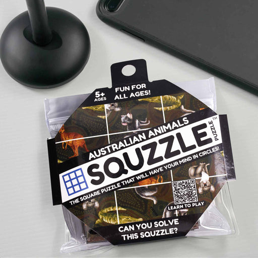 Squzzle Australian Animals puzzle packaging on a light gray surface with a black stand and phone in the background.