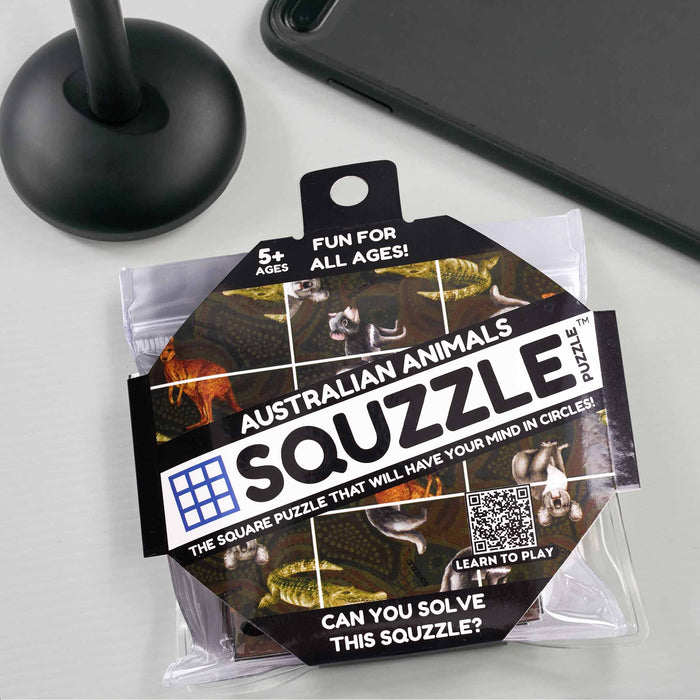 Squzzle Australian Animals puzzle packaging on a light gray surface with a black stand and phone in the background.