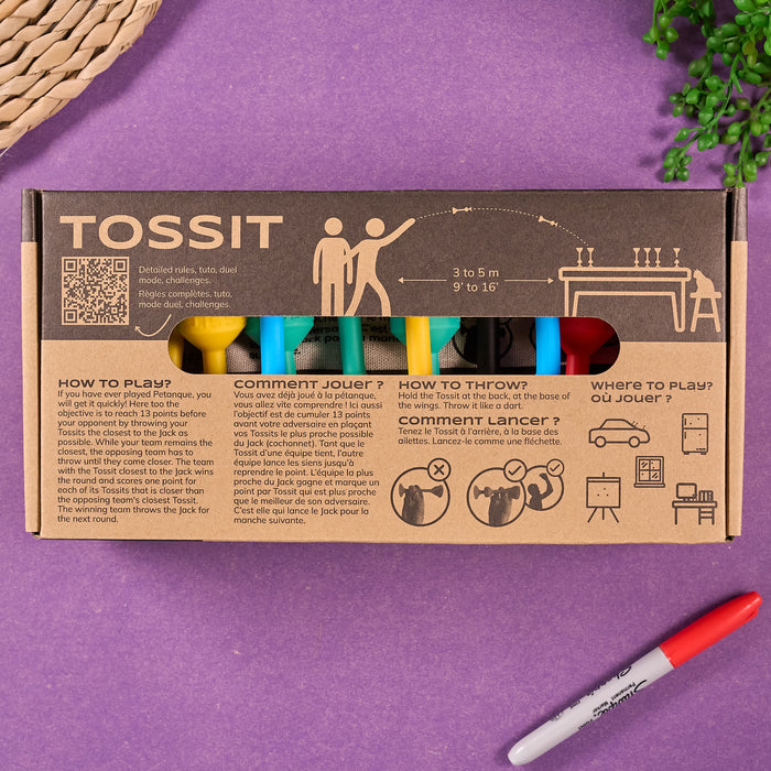 Cardboard packaging of TOSSIT product with colorful elements and text. Tossit game packaging with colorful sticks on a purple surface