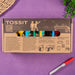 Cardboard packaging of TOSSIT product with colorful elements and text. Tossit game packaging with colorful sticks on a purple surface