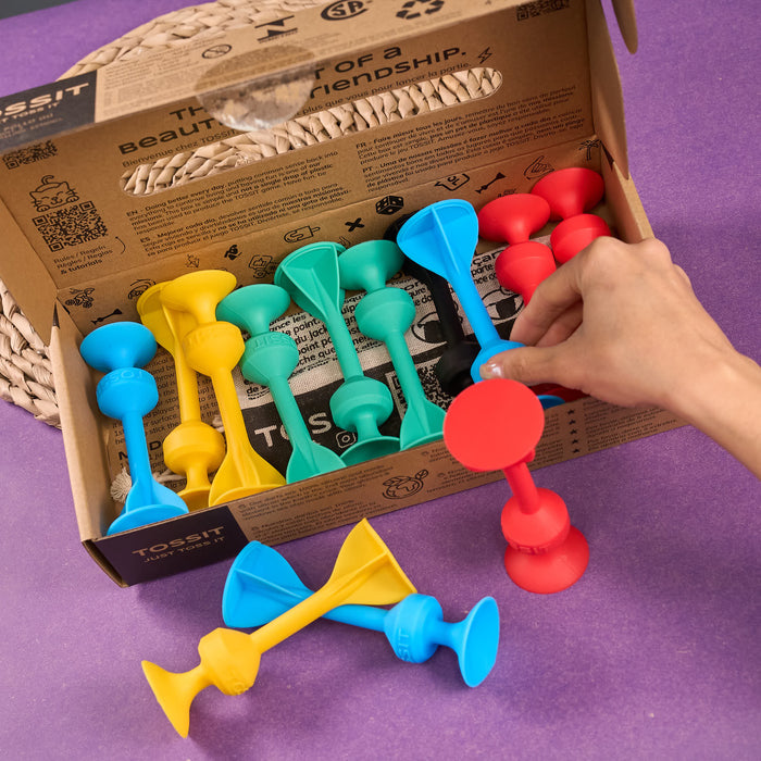 Cardboard packaging of TOSSIT product with colorful elements and text. Colorful dog toys with a cardboard box on a purple background