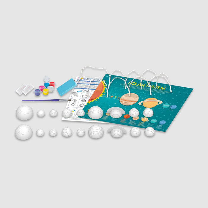 STEAM Powered Kids Solar System model kit with white plastic planet models, small paint pots, a paintbrush, and a printed solar system chart on a light gray background.