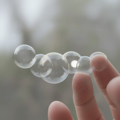 Clear bubbles held between fingers against a blurred natural background