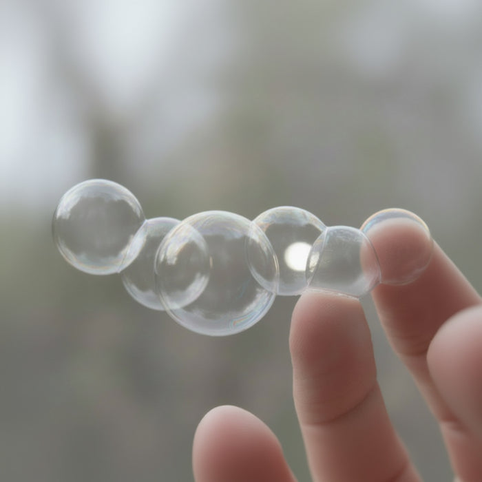 Clear bubbles held between fingers against a blurred natural background