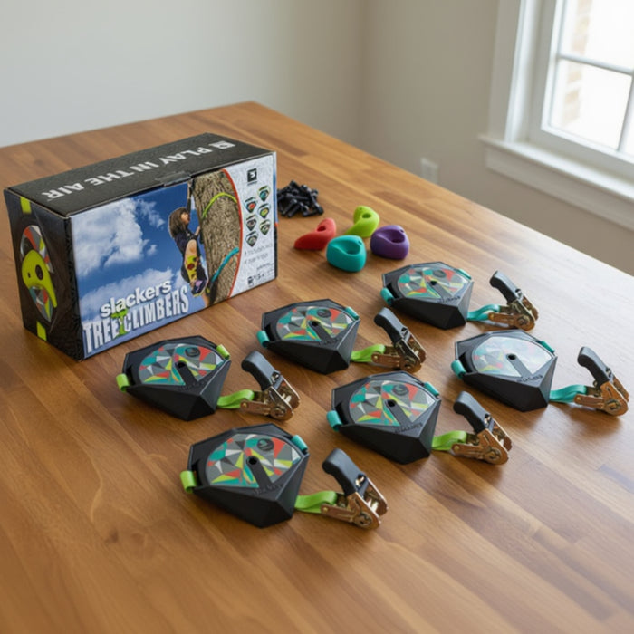 Set of climbing belay devices on a wooden table with packaging in the background.