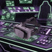 A gray and black virtual reality headset with a padded head strap, resting on a futuristic dark control console with glowing green and purple interface displays.