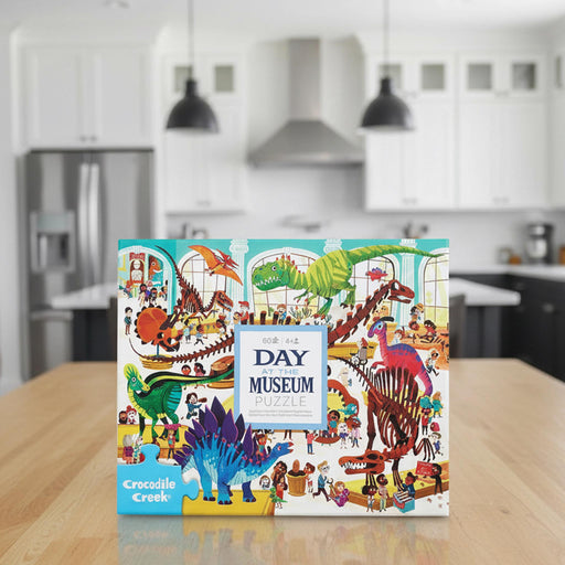 Crocodile Creek Day at the Museum Puzzle box, featuring a colorful, busy illustration of dinosaurs and children exploring a museum.
