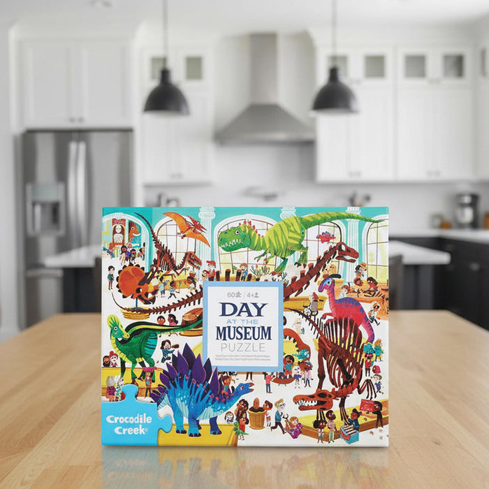 Crocodile Creek Day at the Museum Puzzle box, featuring a colorful, busy illustration of dinosaurs and children exploring a museum.