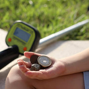 Hand holding coins with a metal detector in the background on grass