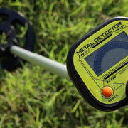 Metal detector with a green screen and orange power button on grass