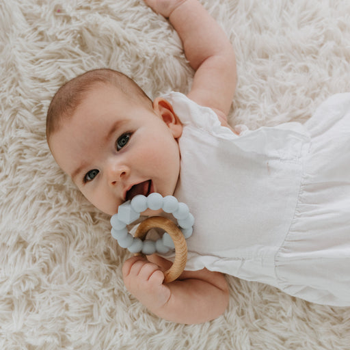 Baby lying on a fluffy white rug holding a teething ring.