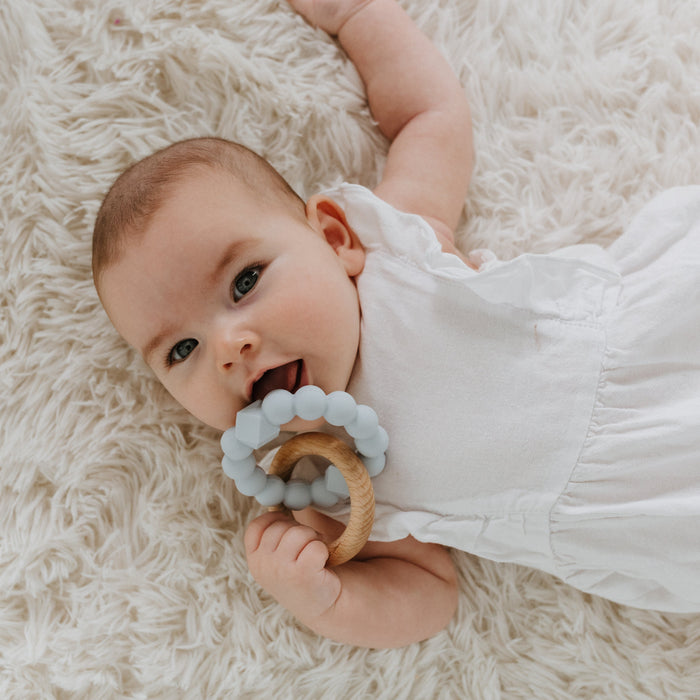 Baby lying on a fluffy white rug holding a teething ring.