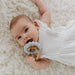 Baby lying on a fluffy white rug holding a teething ring.