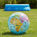 A colorful world map globe resting on green grass, with a blue inflatable pool blurred in the background outdoors.