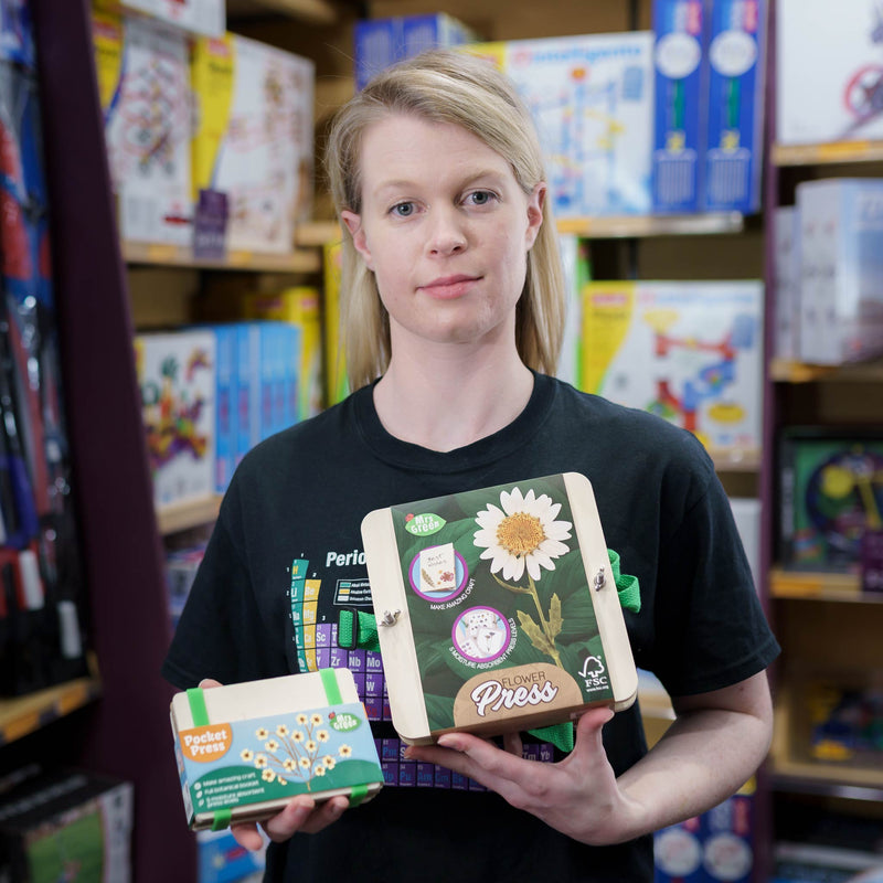  a girl holding a set of pressed flower cards The cards have white paper inserts with pressed flowers on brown kraft backing, and one wooden board has a green ribbon handle and the words 'Mrs Green' printed on it.