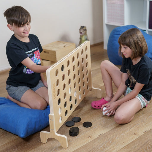 Two children playing the outdoor connect 4 game 'Linkki' by Finska. The game is made of linden plywood with a clear varnish finish and includes black and white wooden discs.